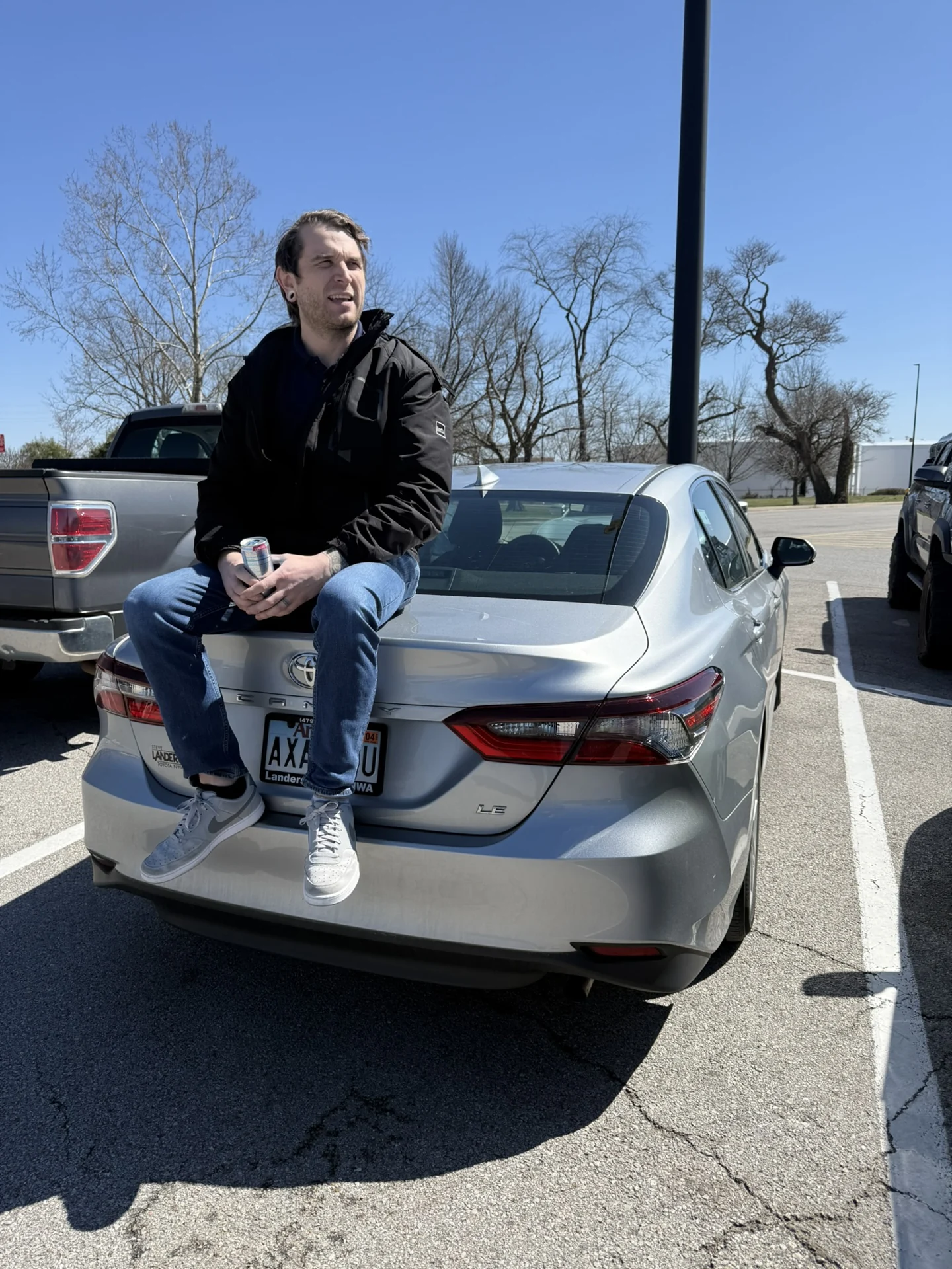 Evan seated on the back of a silver car