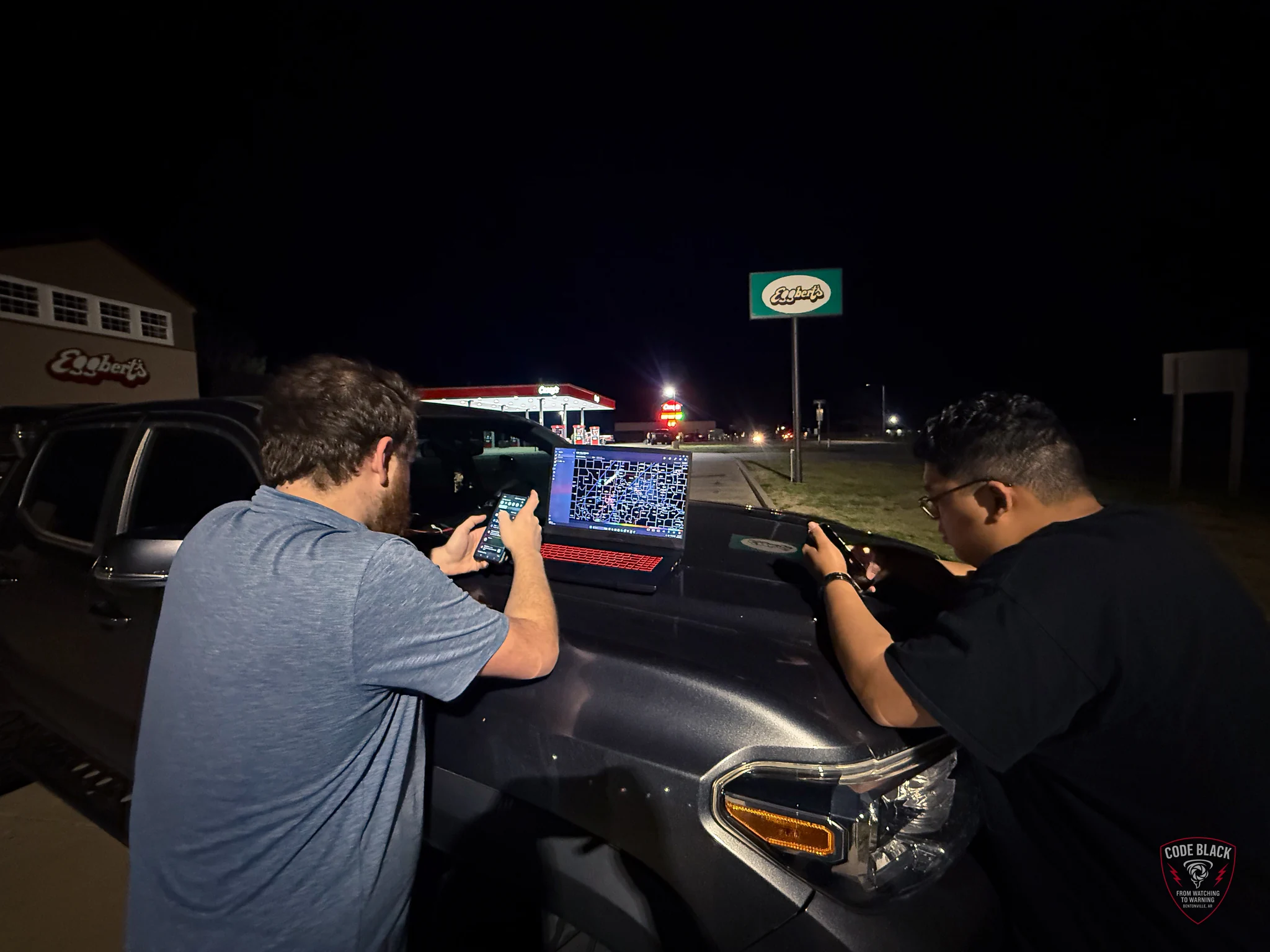 Two people checking screens beside a chase vehicle at night